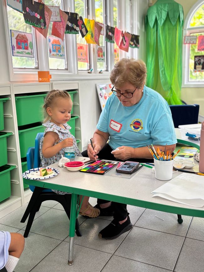 A child and an adult painting at a table in a brightly decorated room.