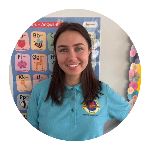Woman in blue shirt smiles in front of a colorful alphabet poster.