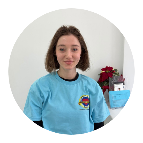 Woman in blue shirt smiles, standing in front of a white wall.
