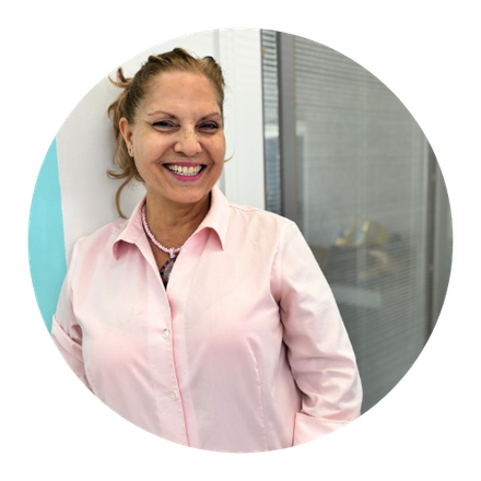 Woman in pink shirt smiles, leaning against a wall in an office setting.