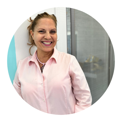 Woman in pink shirt smiles, leaning against a wall in an office setting.