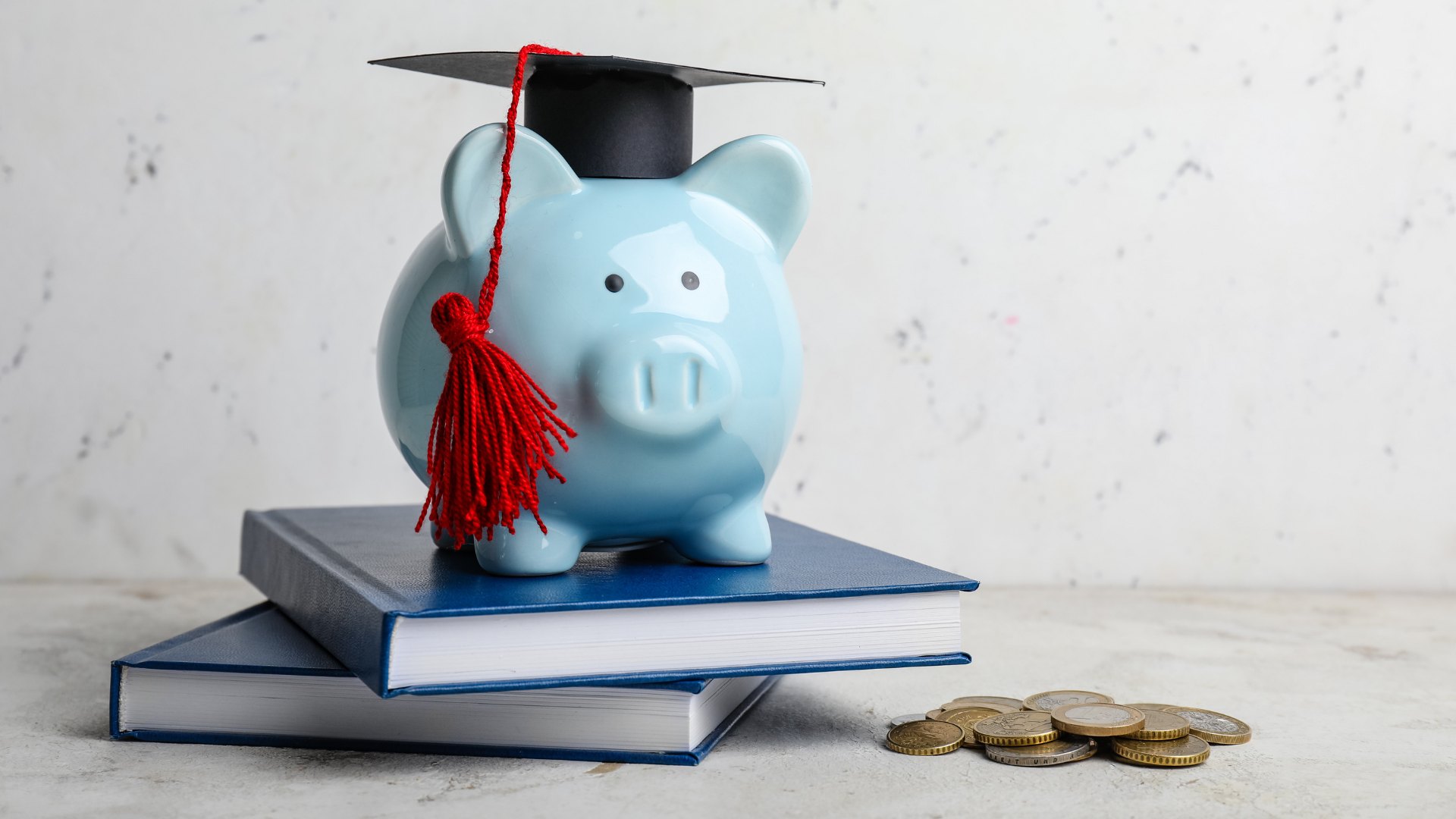 Blue piggy bank with graduation cap on books; coins nearby.