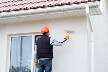 A man is painting the side of a house with a roller.