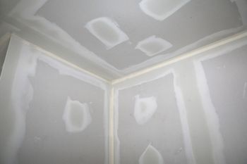A corner of a room with drywall walls and a ceiling.