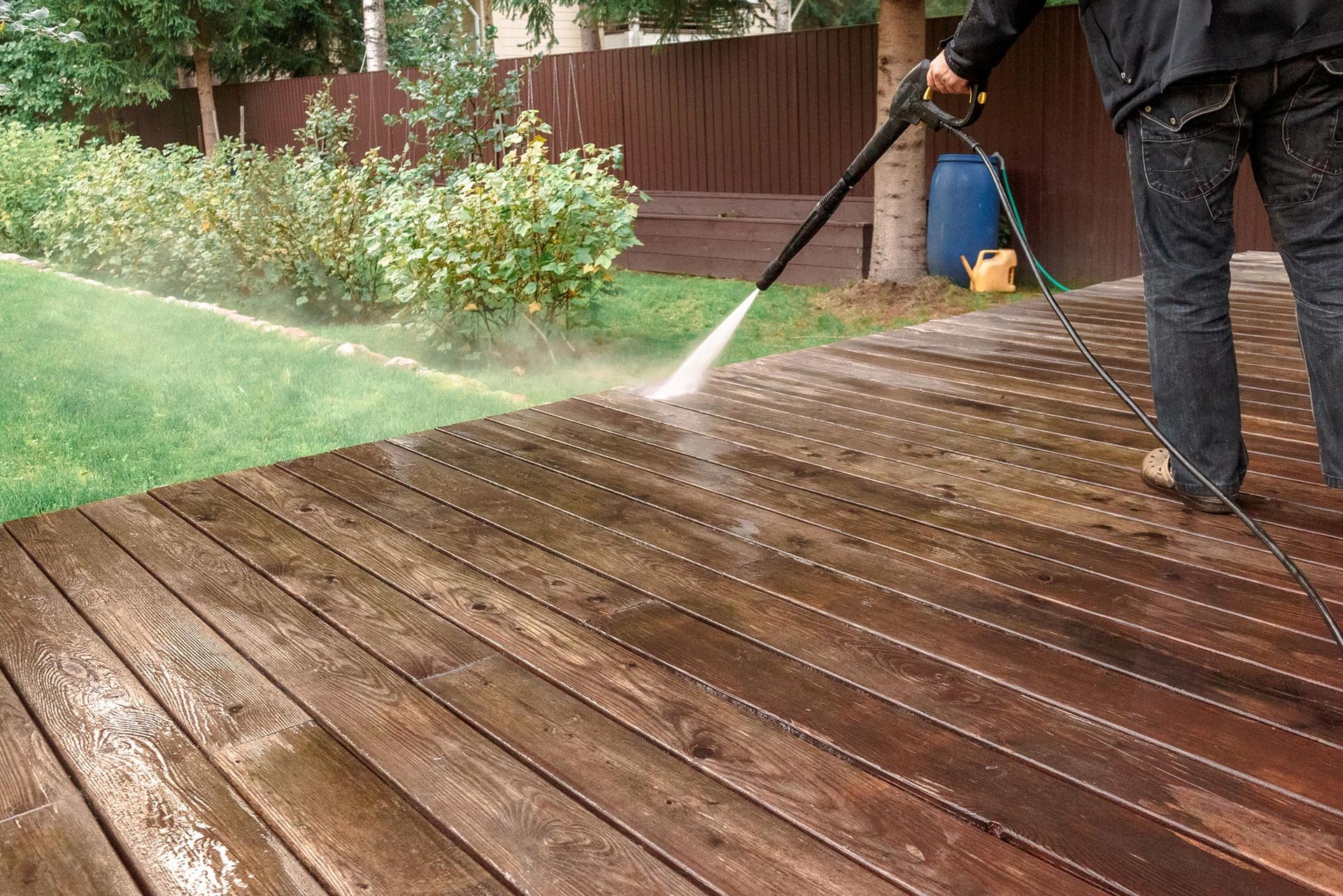A man is using a high pressure washer to clean a wooden deck.