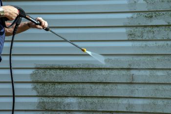 A man is cleaning the side of a house with a high pressure washer.