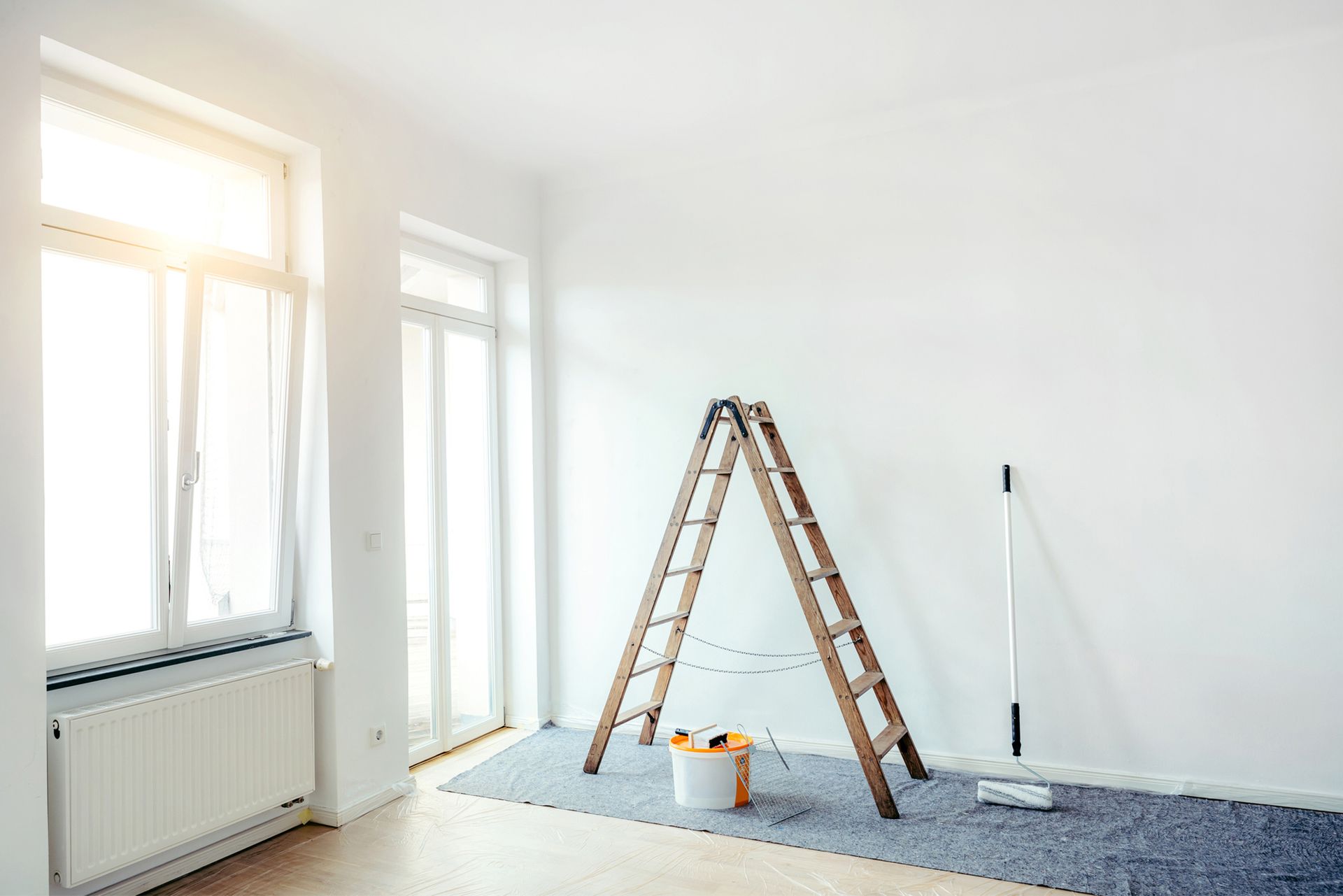 An empty room with a ladder, bucket of paint and mop.