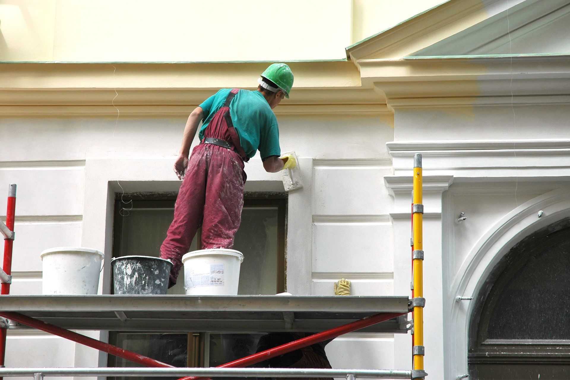 A man is painting the side of a building on a scaffolding.