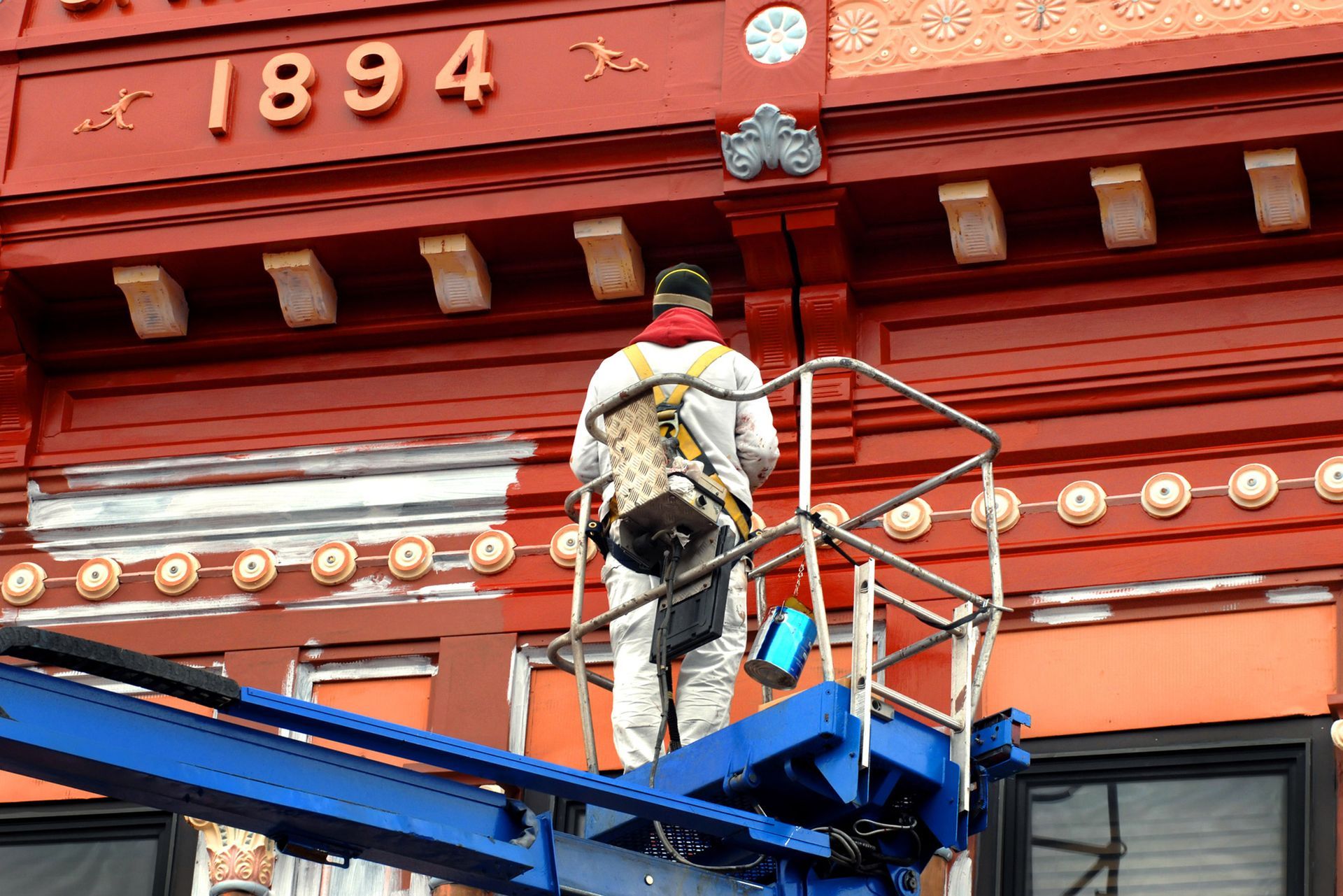 A man is painting a building with the year 1894 on it. A man is painting a building with the year 1894 on it.