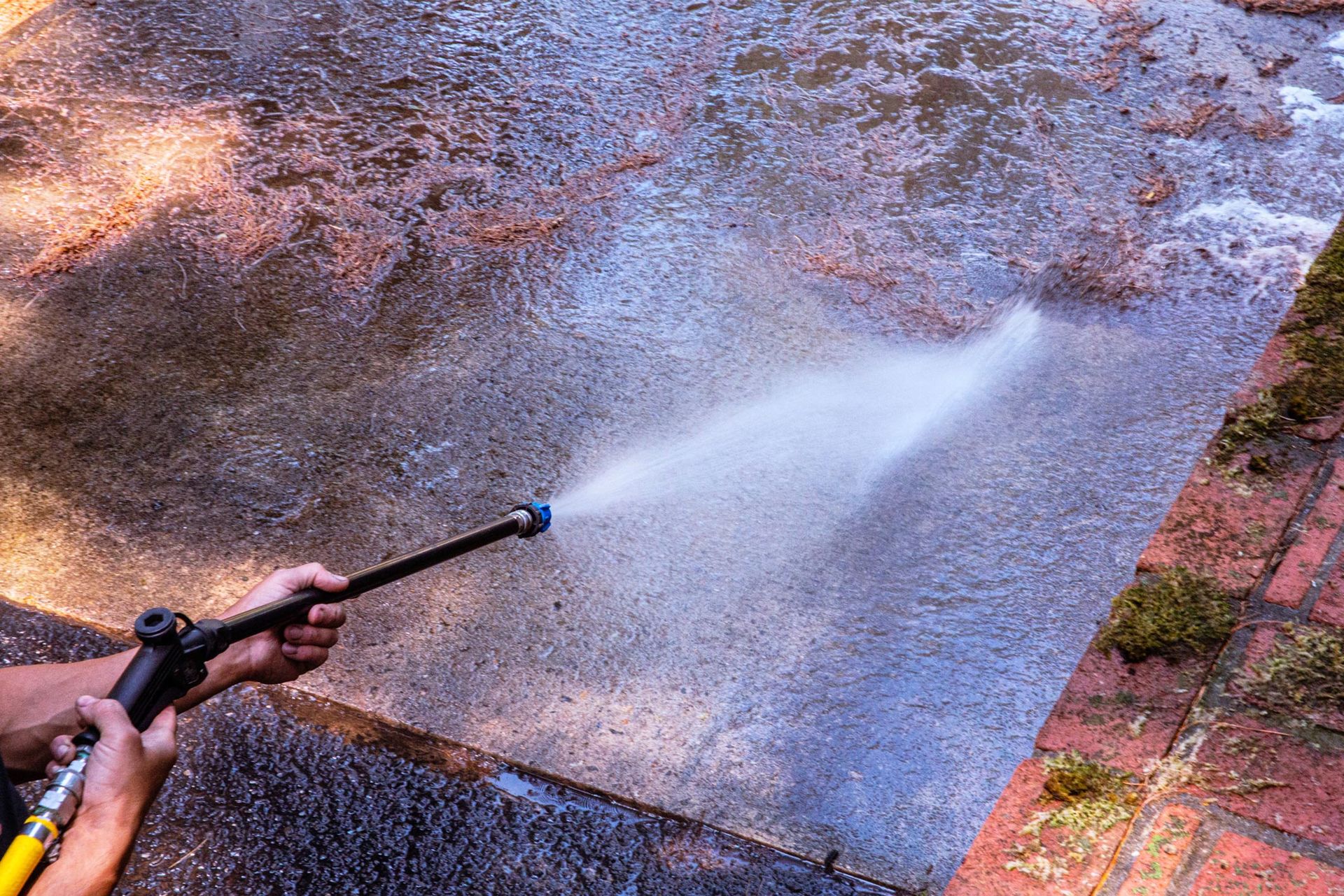 A person is using a high pressure washer to clean a sidewalk.