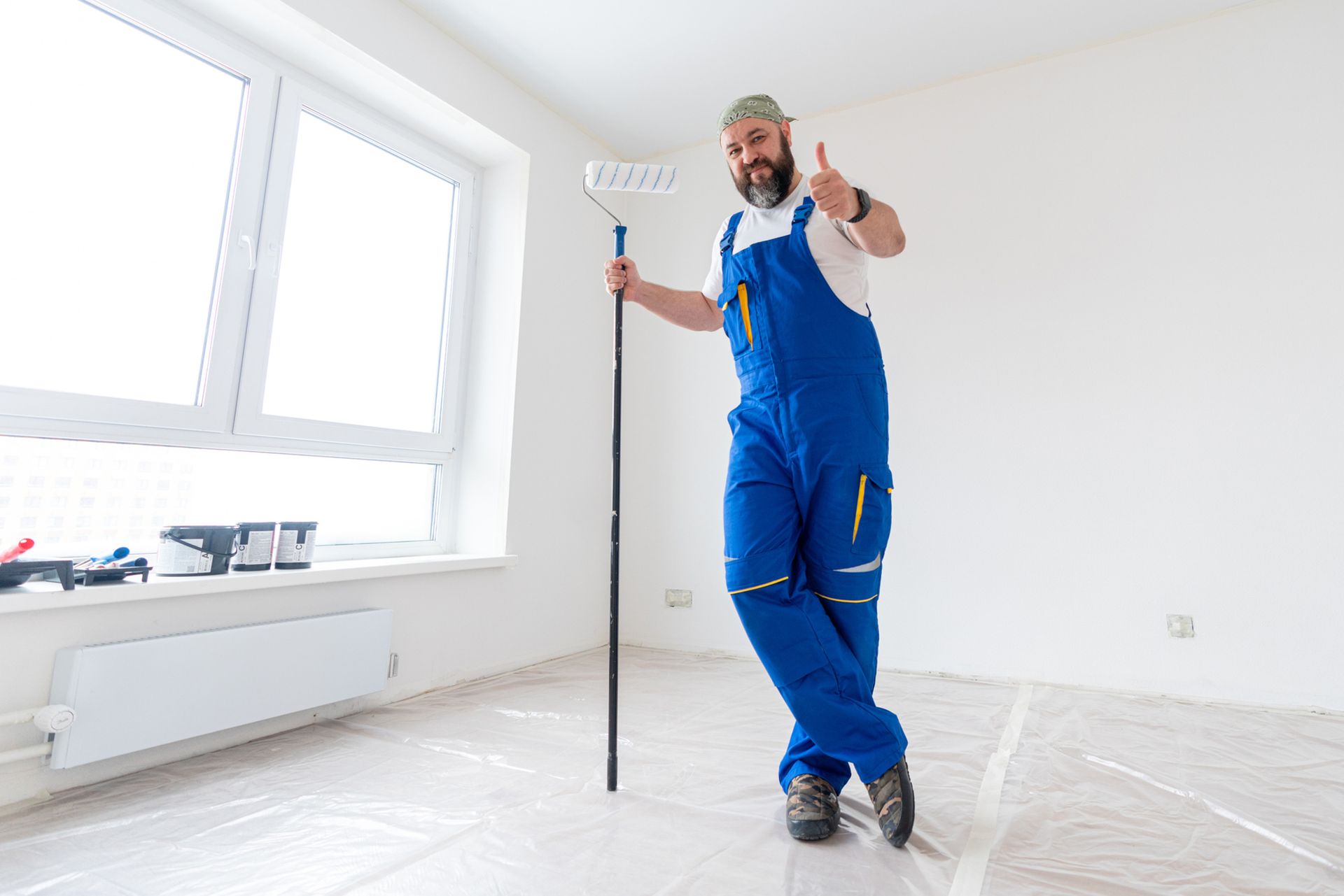 A man is standing in an empty room holding a paint roller and giving a thumbs up. A man is standing in an empty room holding a paint roller and giving a thumbs up.