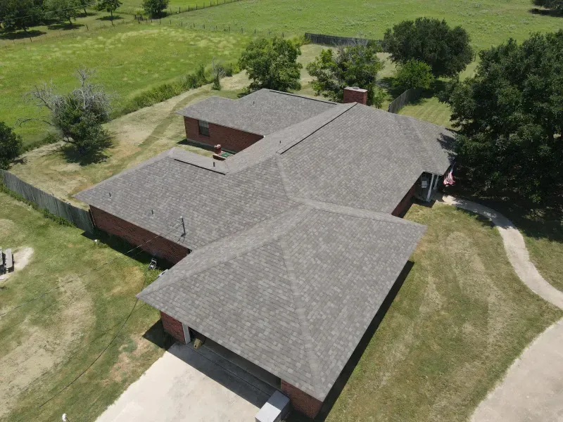 An aerial view of a house with a roof that is surrounded by grass and trees.