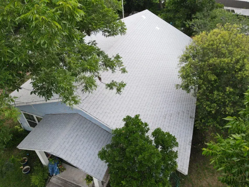 An aerial view of a house with a white roof surrounded by trees.