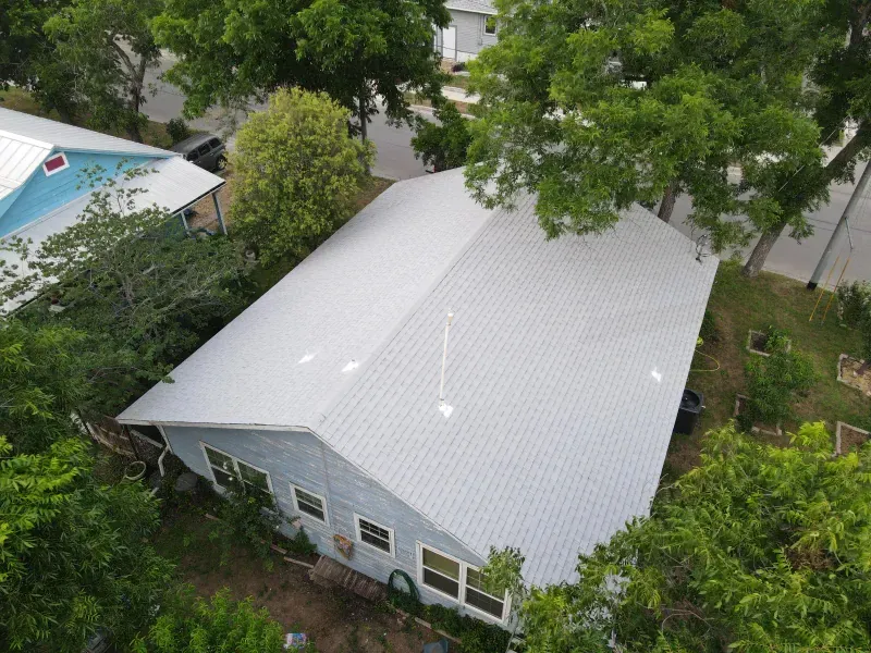 An aerial view of a house with a white roof surrounded by trees.