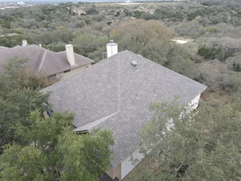 An aerial view of a house with a roof that is surrounded by trees.