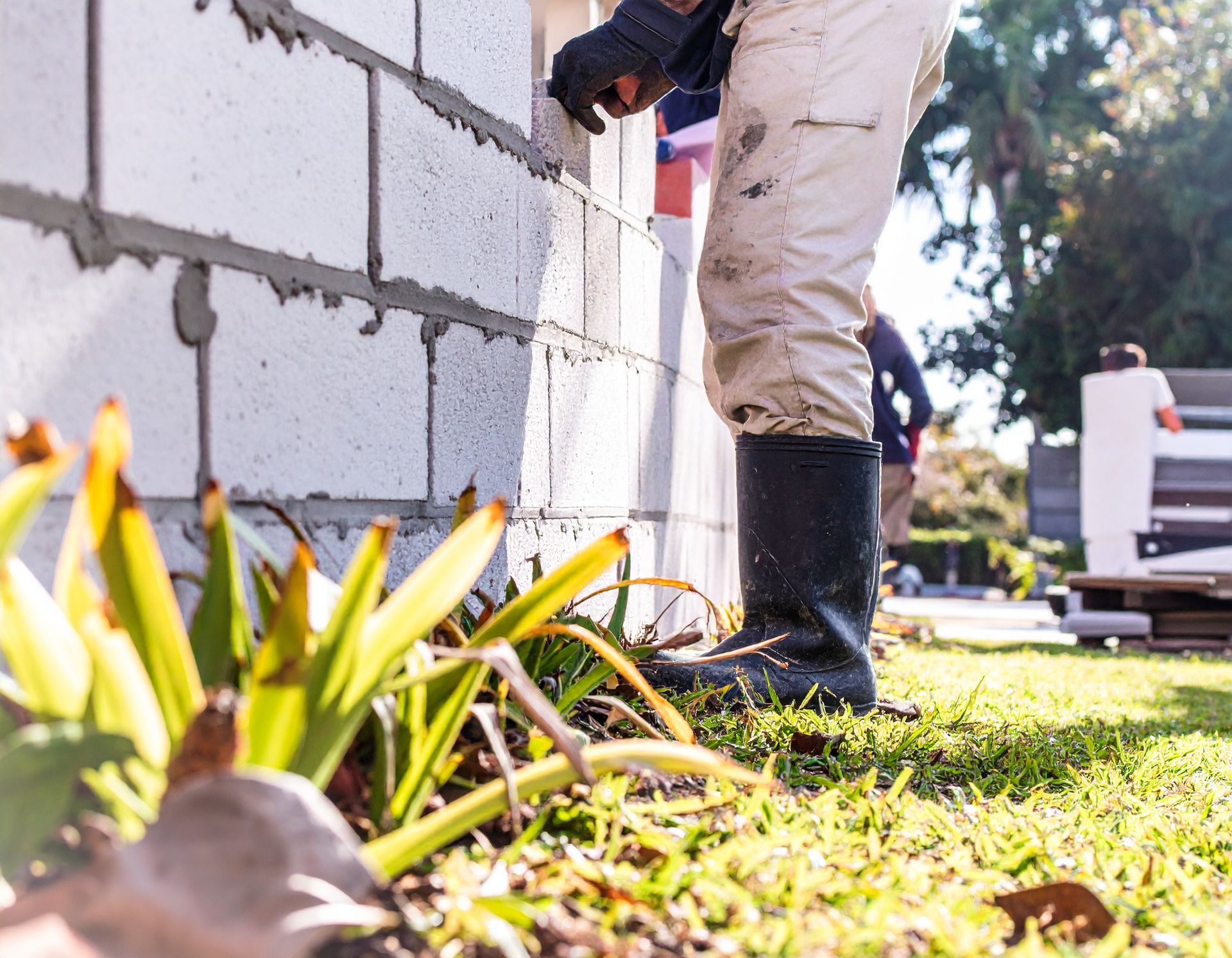Worker standing beside a freshly built CMU wall along a lawn in Coral Gables.
