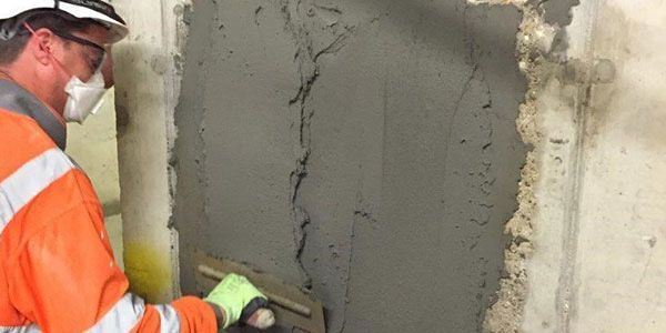 Technician troweling cement patch to repair a spalled concrete wall in Coral Gables.