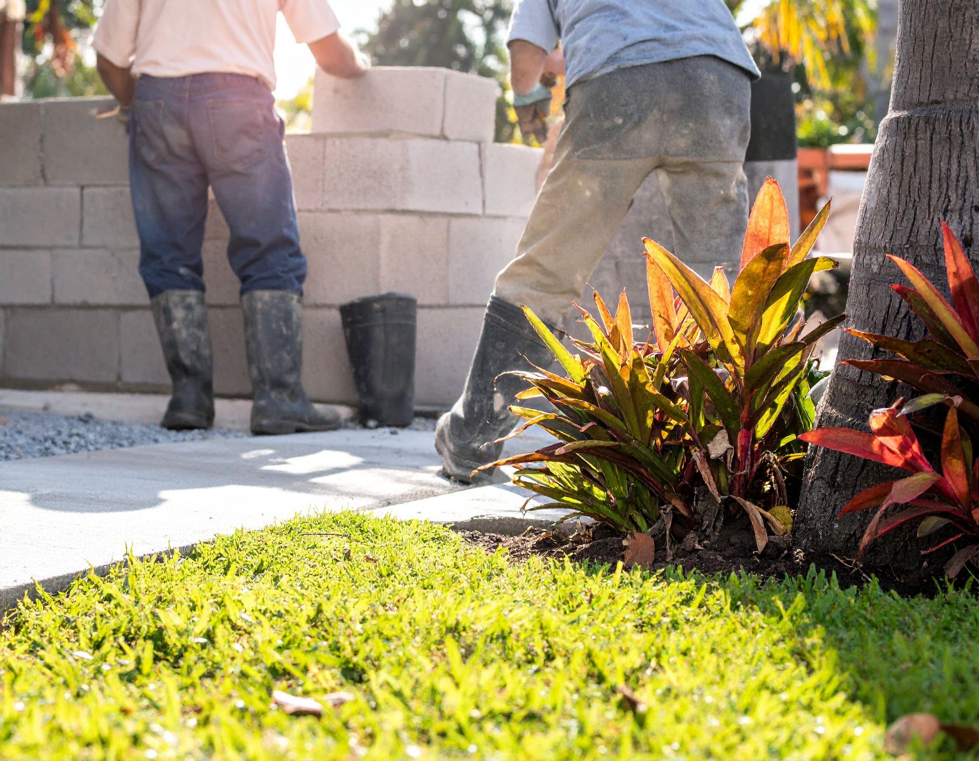 Crew laying concrete blocks for a home wall beside tropical landscaping in Coral Gables.