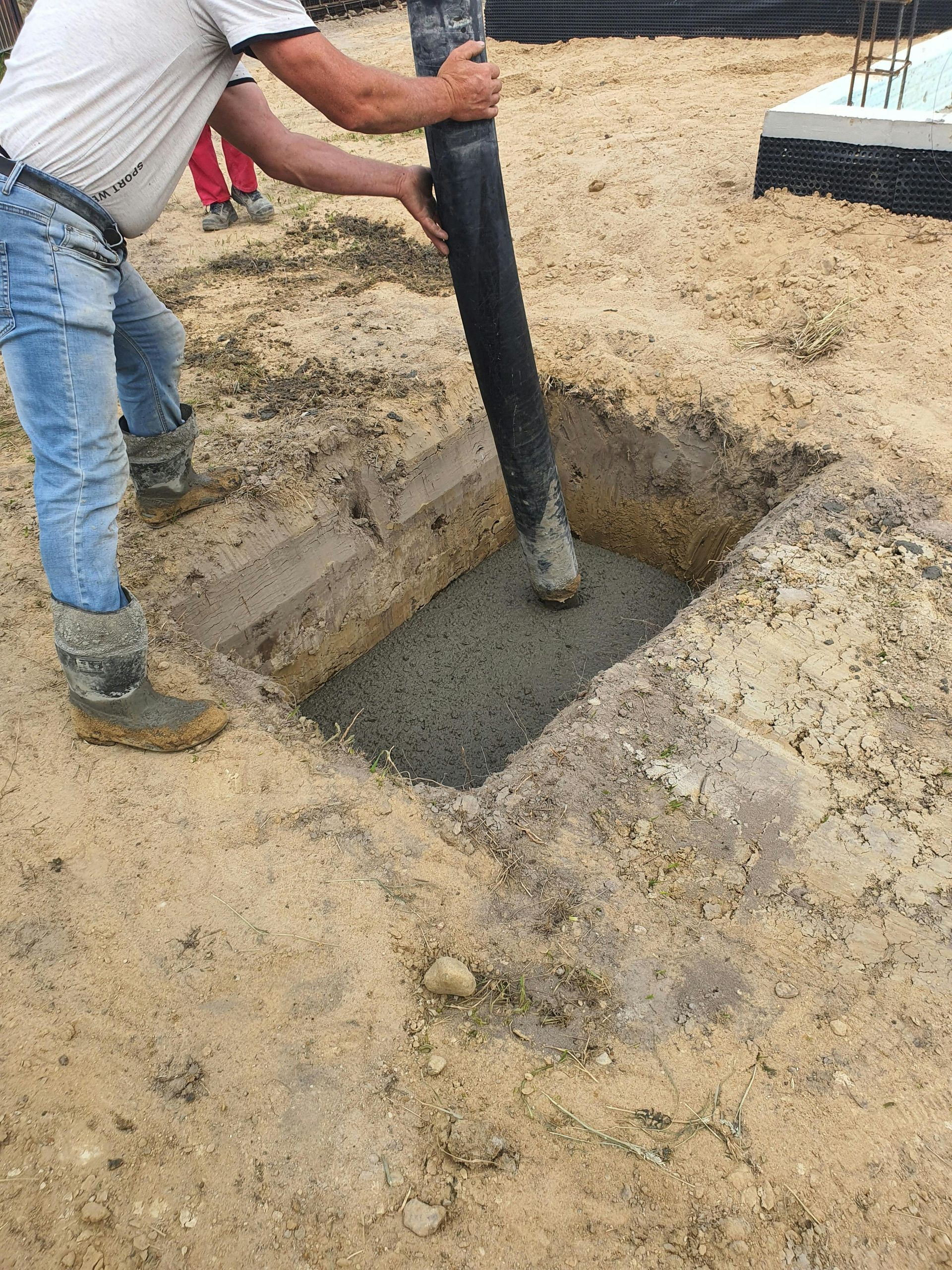 Worker placing concrete with a pump hose into footing trench for a slab foundation in Coral Gables.