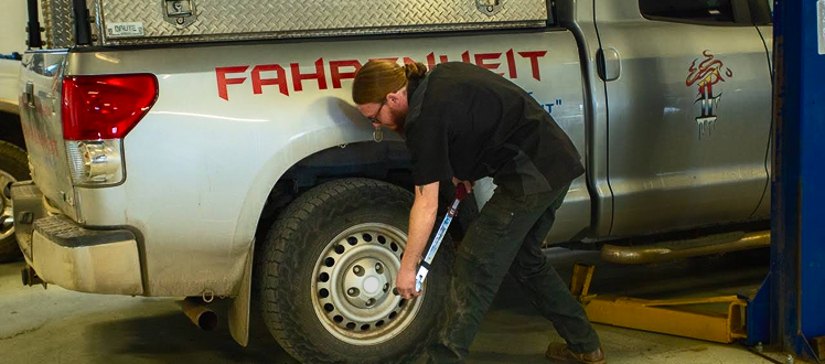 A person in a black uniform uses a torque wrench on the wheel of a silver pickup truck in an auto repair shop. | Performance Automotive Repair
