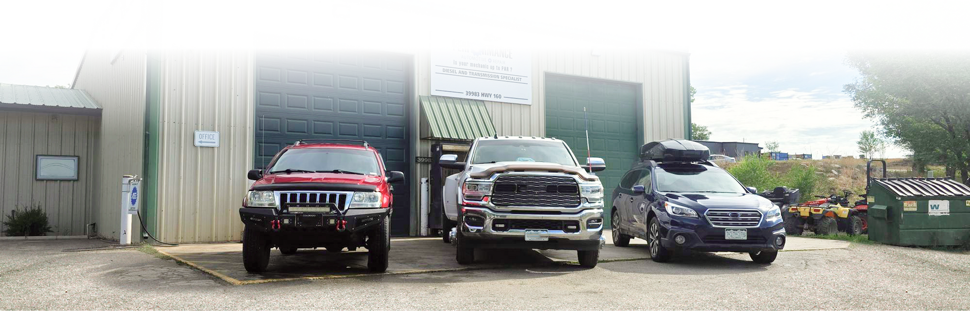 Three vehicles, a red SUV, a silver truck, and a dark sedan, parked in front of a warehouse building with large doors. | Performance Automotive Repair