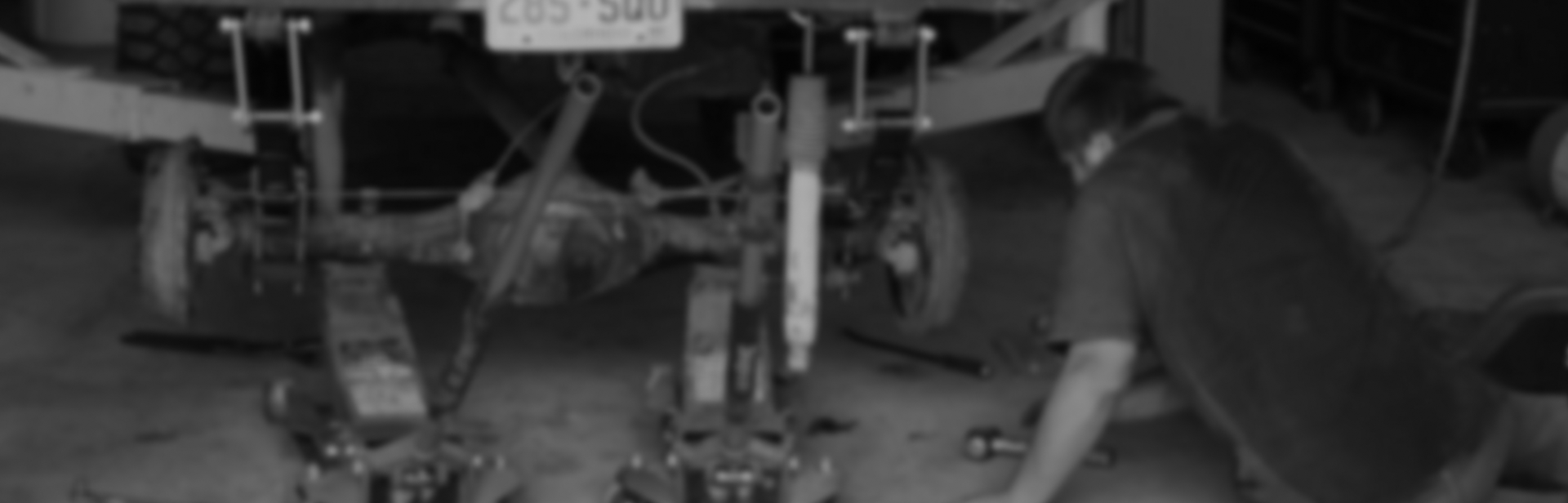 A mechanic works underneath the rear of a vehicle raised on jack stands in an auto shop | Performance Automotive Repair