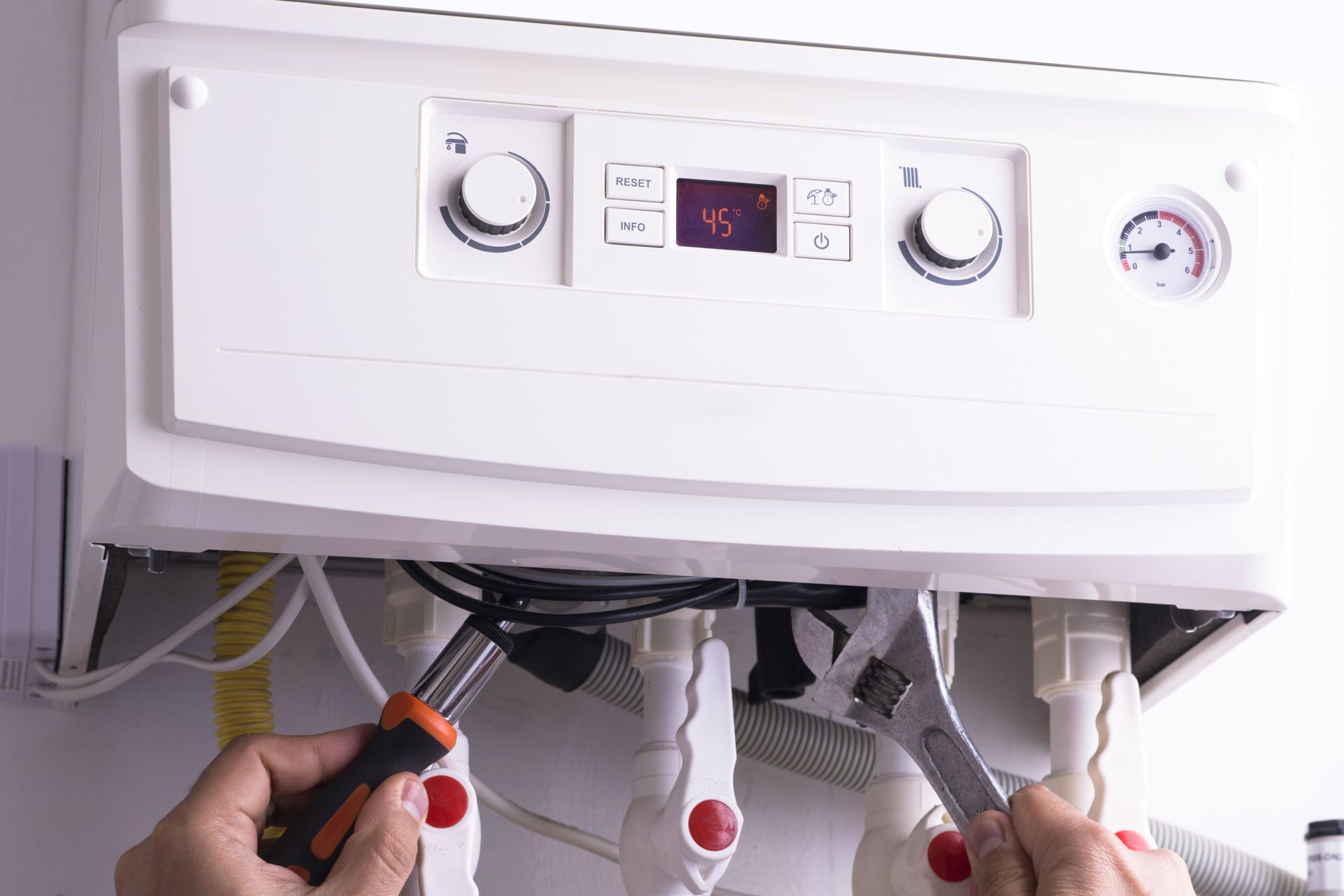 Person working on pipes under a white boiler with control panel and knobs Person working on pipes under a white boiler with control panel and knobs