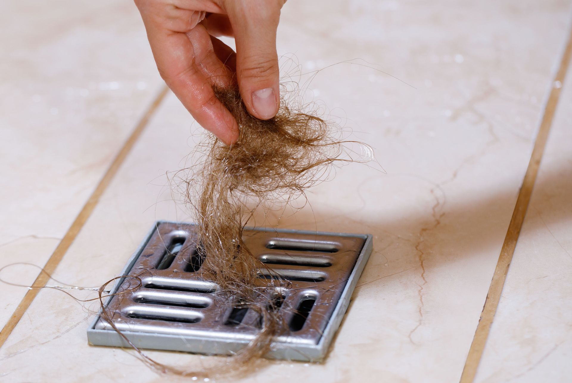 Hand pulling clump of hair from a bathroom floor drain on tiled floor Hand pulling clump of hair from a bathroom floor drain on tiled floor