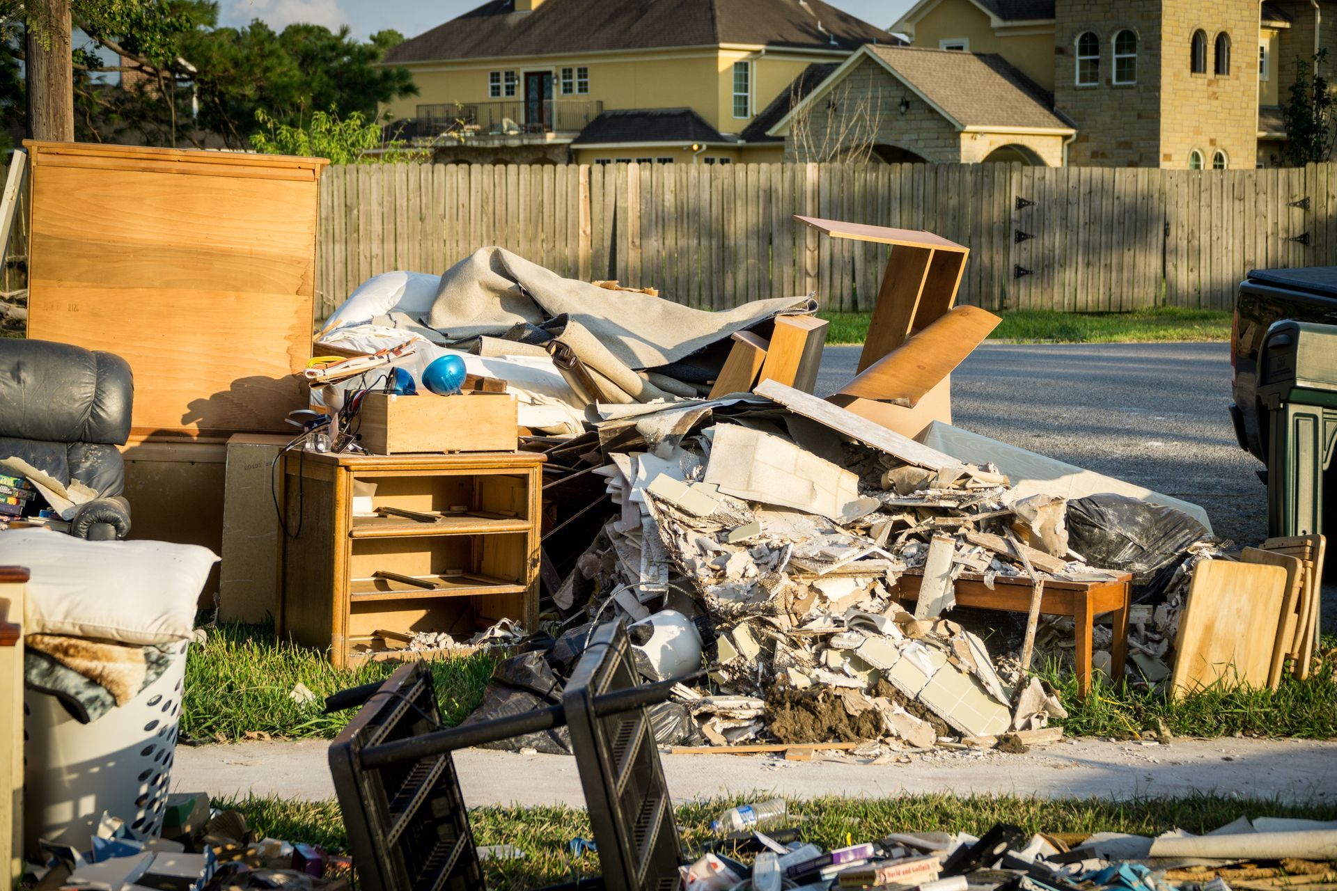 Pile of discarded furniture and debris on a suburban street. Includes cabinets, a chair, and a broken table.