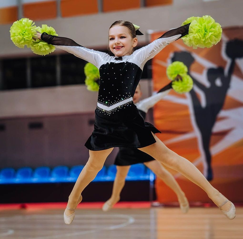 Two cheerleaders are jumping in the air while holding pom poms