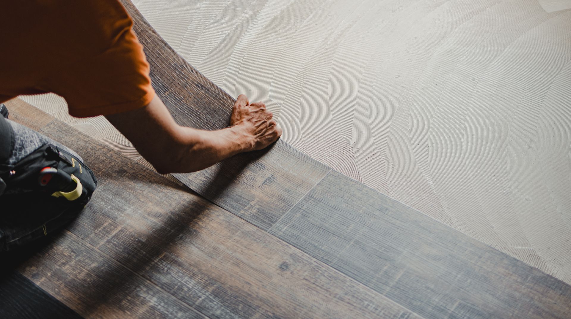 Person installing light-colored flooring, placing a new plank next to existing dark flooring.