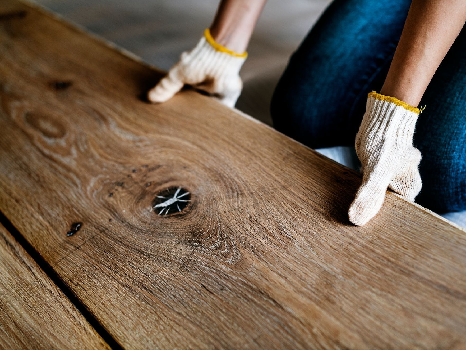 Person wearing gloves installing wooden floor plank.