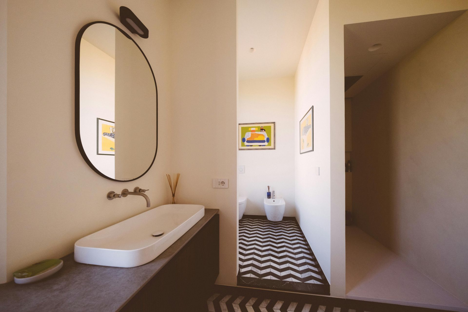 Bathroom with oval mirror, rectangular sink, and patterned rug. Light-colored walls and artwork.
