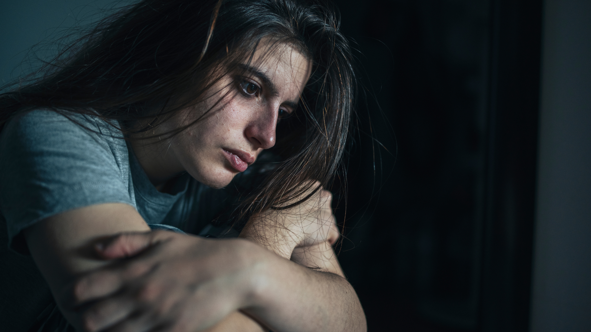 A woman is embracing herself in a dimly lit room.