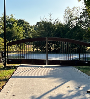 A wooden gate is open to a driveway with trees in the background.