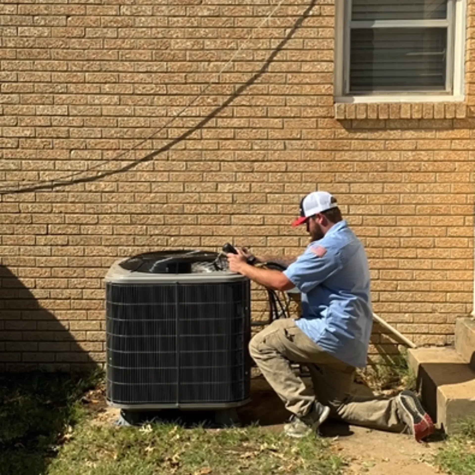 A man is working on an air conditioner outside of a brick building.