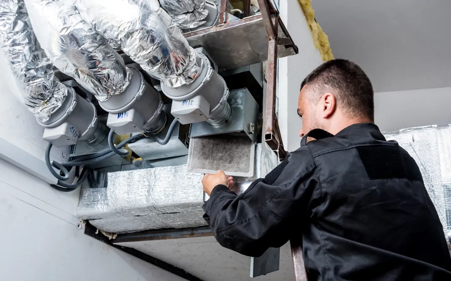 Finnegan’s Heating Air Conditioning -  A man is working on a ventilation system in a building.