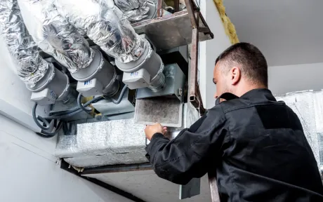 Finnegan’s Heating Air Conditioning - A man is working on a ventilation system in a building.