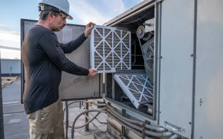 Finnegan’s Heating Air Conditioning - A man is holding a filter in front of an air conditioner.