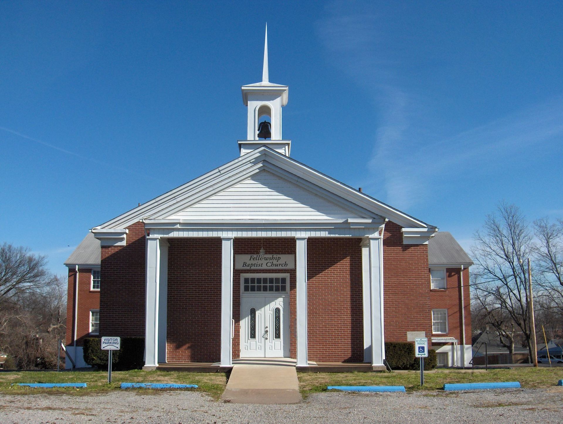 Red brick church with white pillars, steeple, and blue sky.
