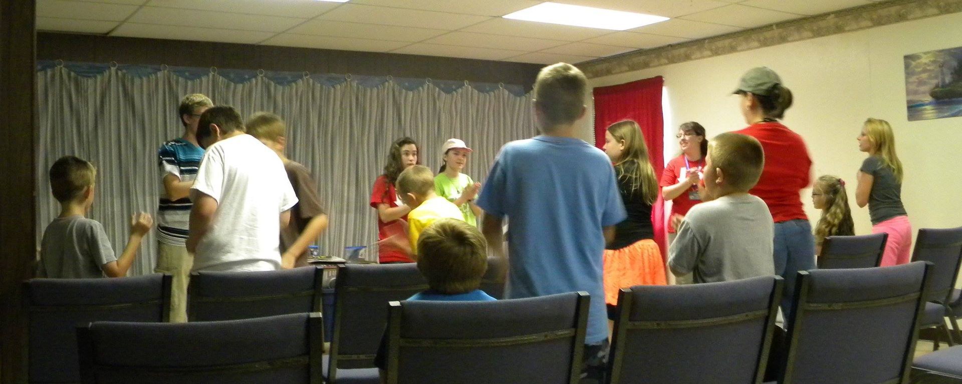 A group of people standing and talking in a room with rows of chairs.
