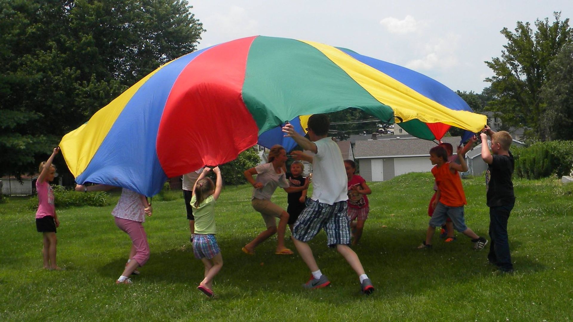 Children playing with a colorful parachute on a grassy field; lifting the fabric.