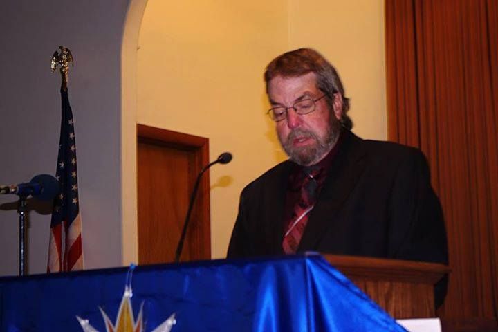 Man in glasses speaking at a podium with an American flag to the left.