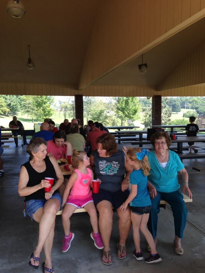 People sitting and standing under a pavilion with picnic tables; some holding red cups.