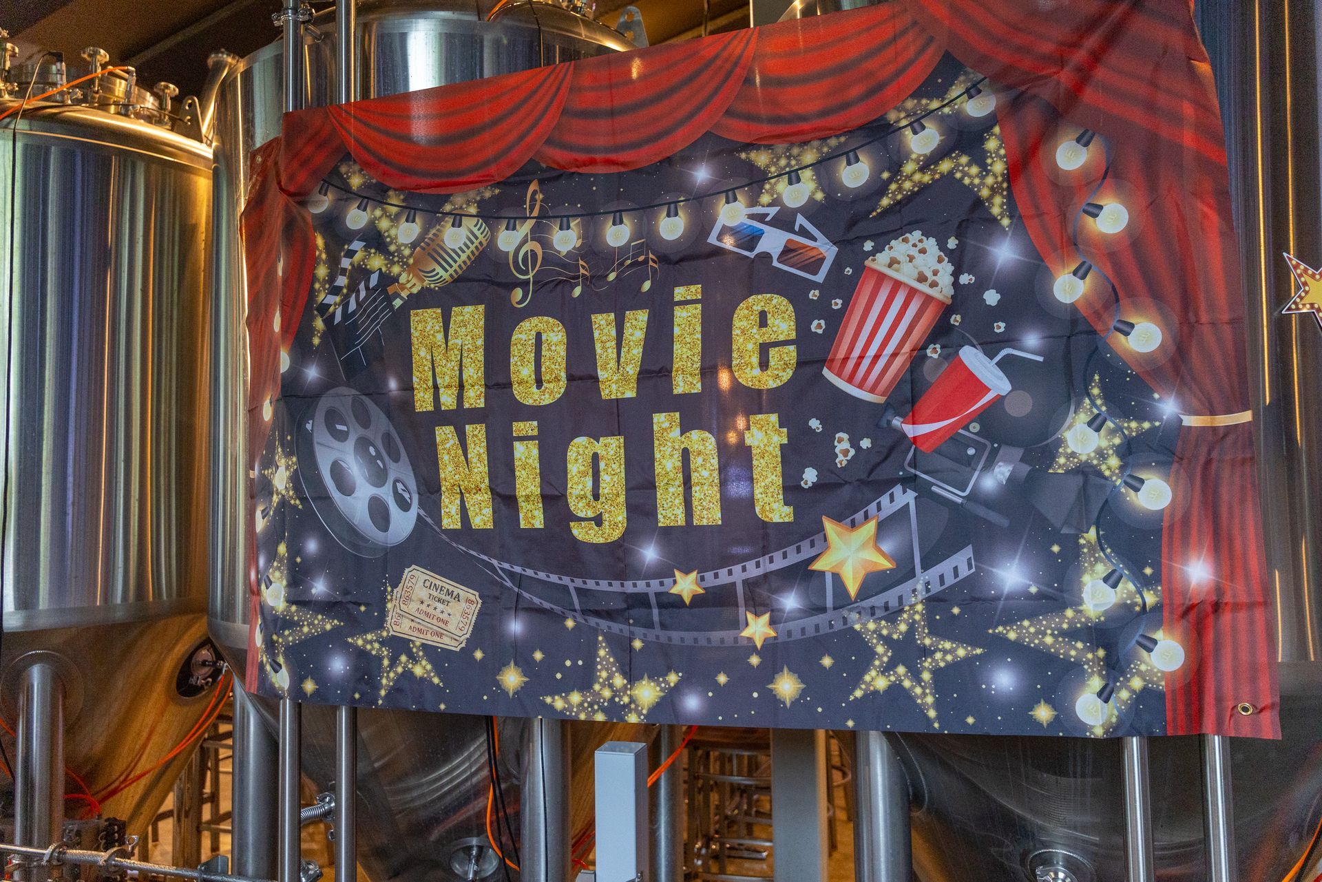 Movie Night banner with film reel, popcorn, and stars in brewery setting.