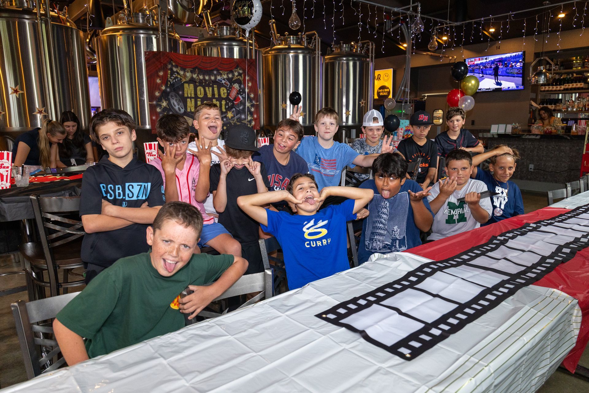 Group of kids making funny faces at a birthday party, sitting around a table with filmstrip decor.