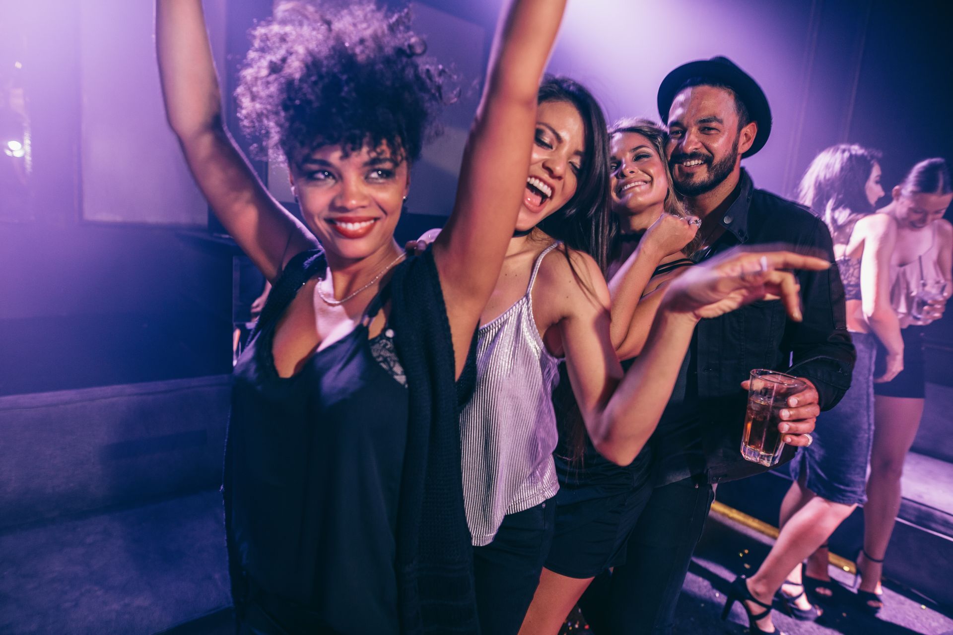 People dancing and smiling in a bar under purple lighting.