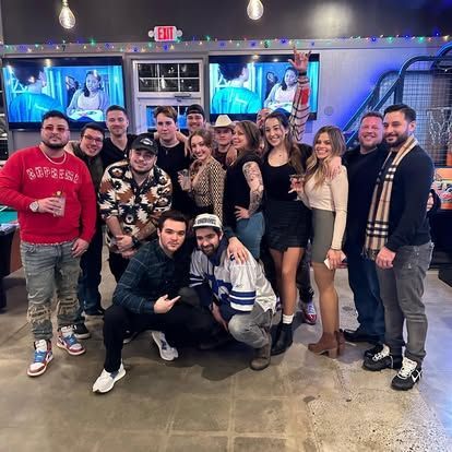 Group of people smiling and posing in a bar; some holding drinks.