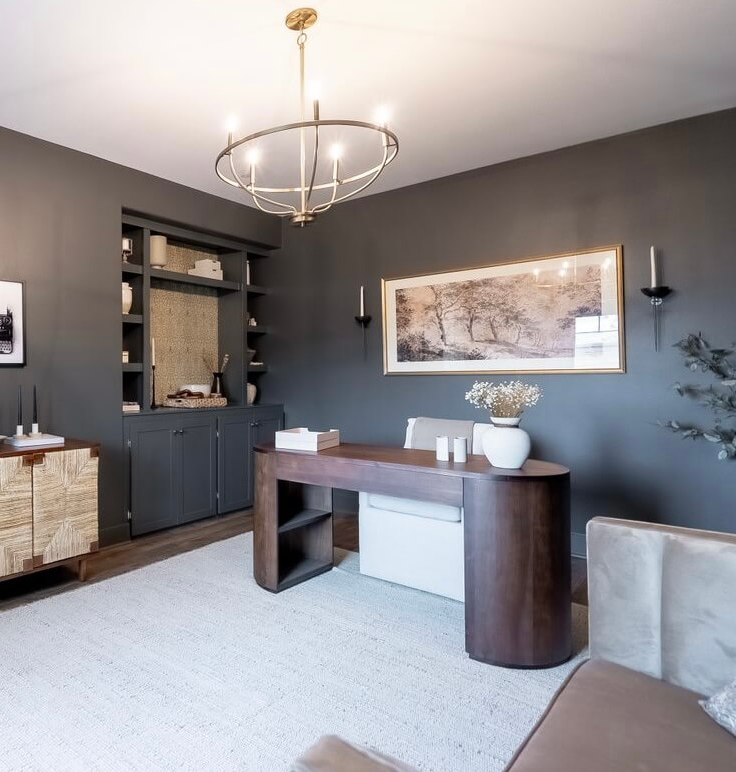 Elegant home office with dark gray walls, a wooden desk, and a cream-colored rug.