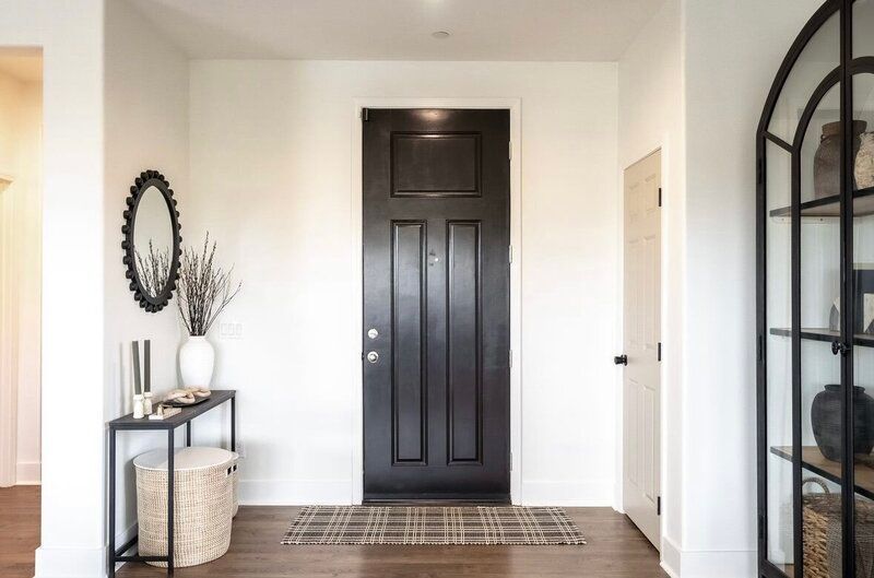 Entryway with black door, white walls, console table, and arched shelf.